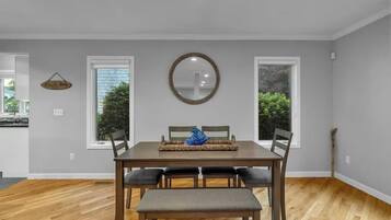Un comedor con una mesa de madera, cuatro sillas y un banco. Hay dos ventanas con vistas a la vegetación exterior.