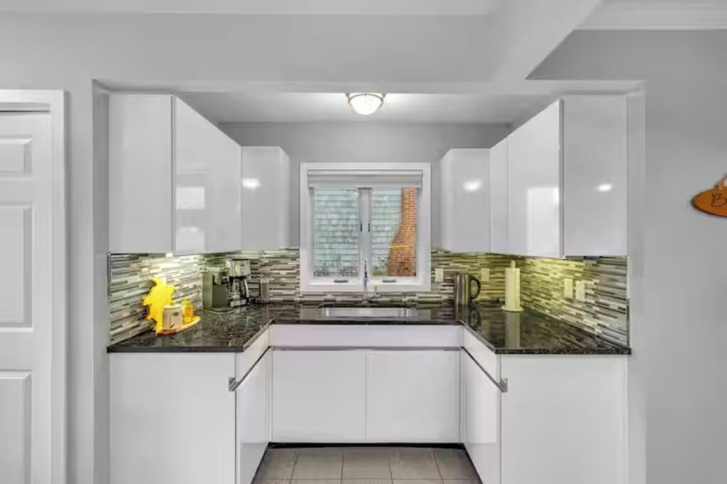 Una cocina moderna con armarios blancos, encimera negra y una ventana con persianas.