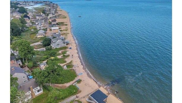 An aerial view of a coastal residential area with houses along the beach, a clear sky, and calm sea. - Beachside Bliss w/ Game Room, Gym & Golf Green (Westbrook)