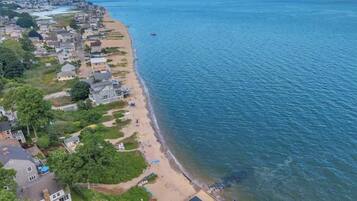 An aerial view of a coastal residential area with houses along the beach, a clear sky, and calm sea.