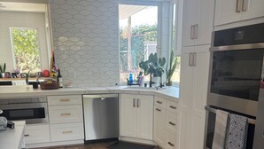 Una cocina moderna con armarios blancos, piso de madera y un amplio ventanal que proporciona luz natural.
