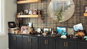 Un mueble de madera oscura con varios cajones, un espejo y varios objetos decorativos, incluyendo figuritas y cuadros enmarcados.