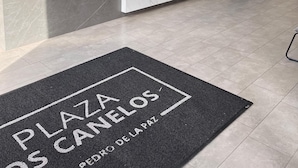 Un área de recepción moderna con mostrador de mármol, una paleta de colores blanco y negro y un letrero que dice "Plaza de los Caneles".