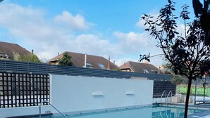 Una piscina con plataforma de baldosas, una planta en maceta y una cerca al fondo.