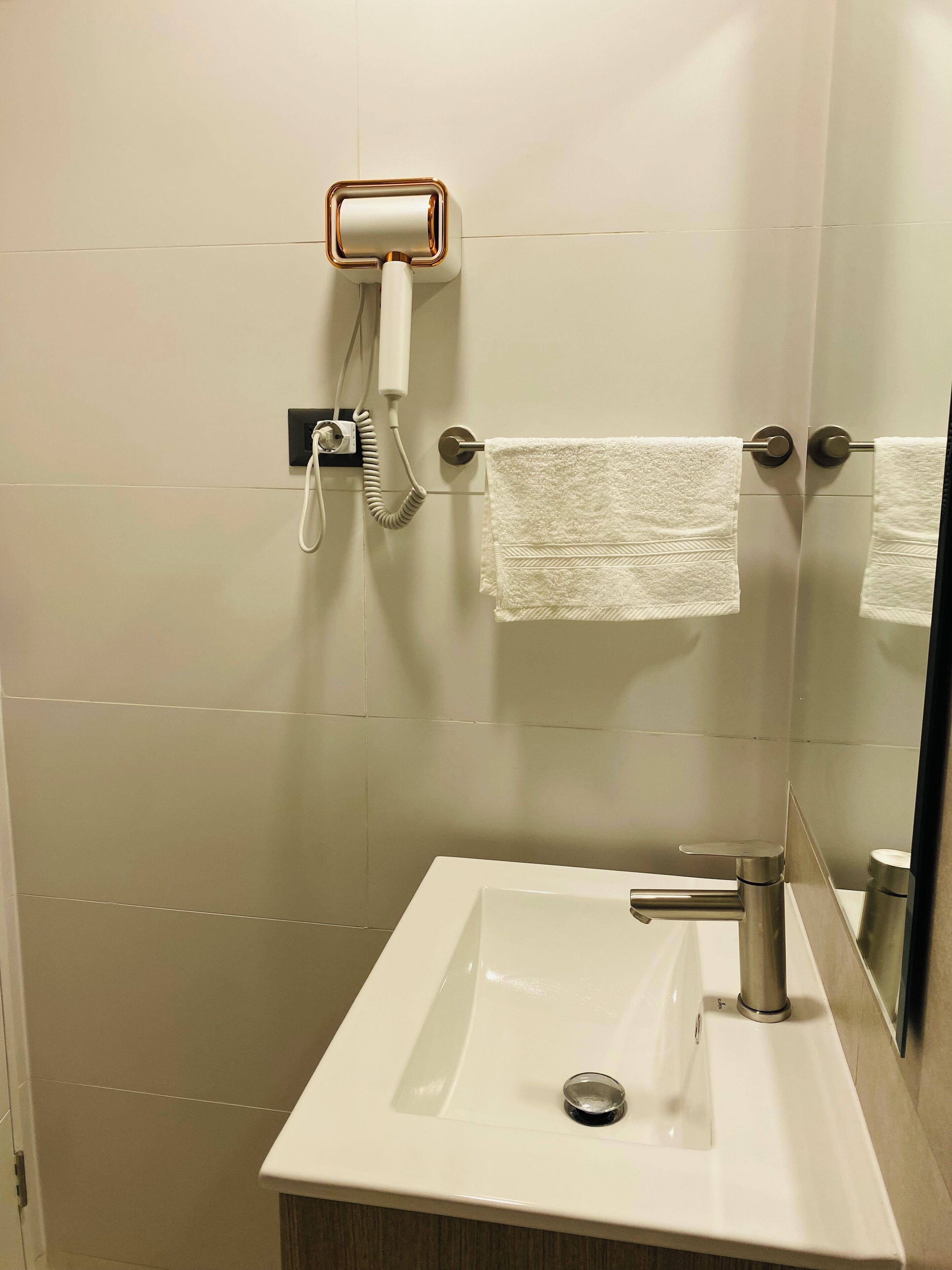 A bathroom with a white sink, a towel rack with two towels, a hairdryer, and a mirror.