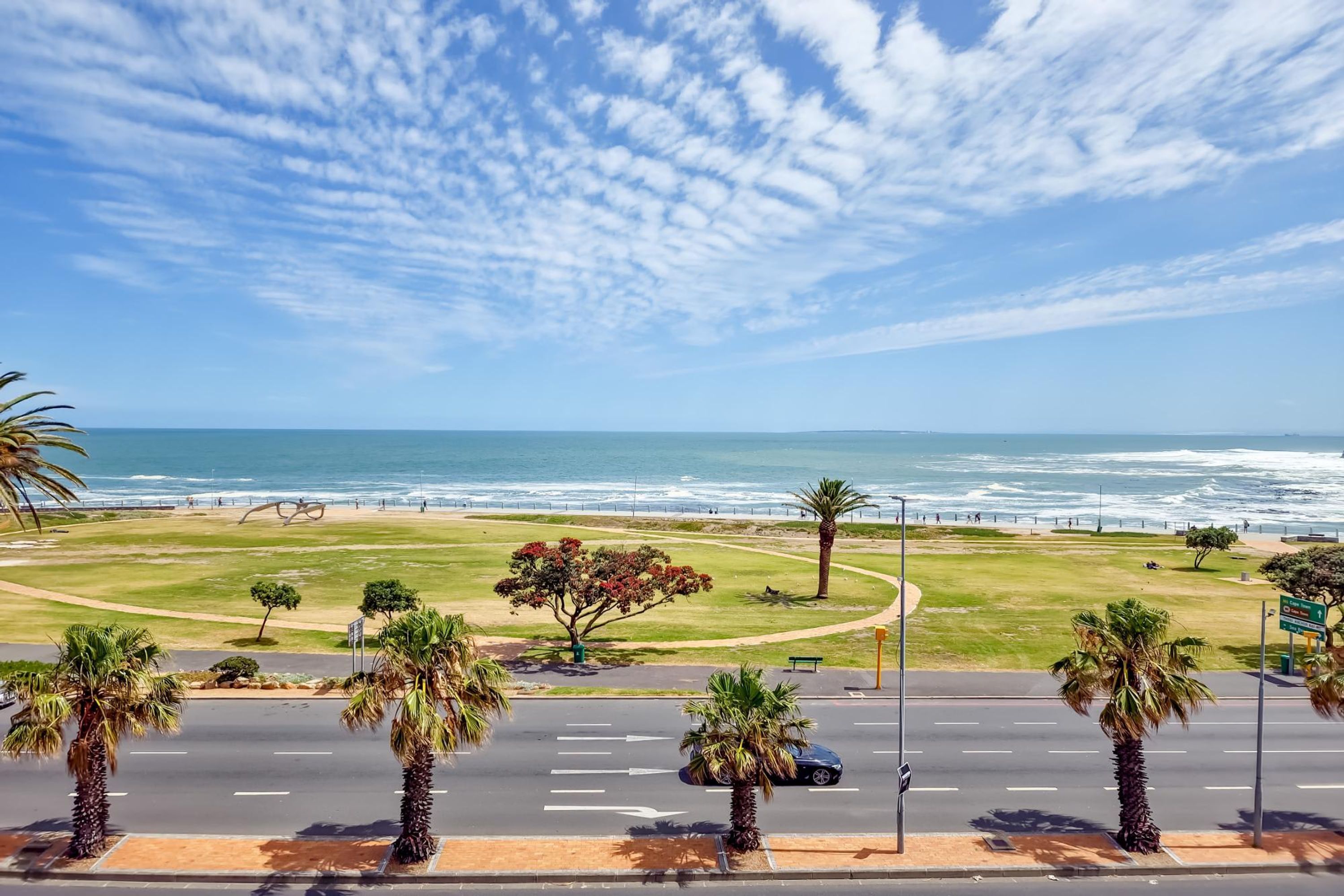 A coastal road with palm trees, a beach, and the ocean in the background.