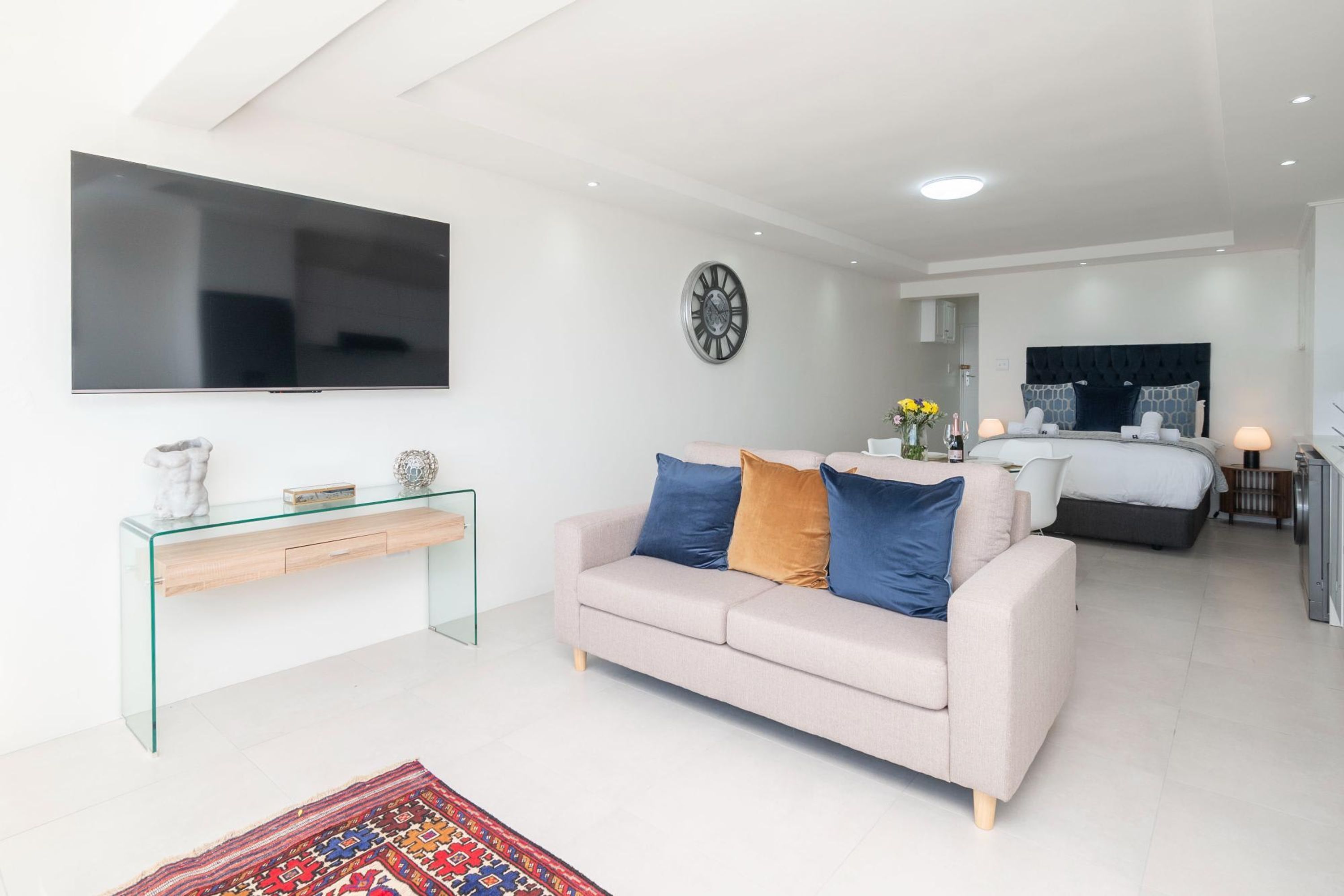 A modern living room with a sofa, a glass console table, a flat-screen TV, and a large clock on the wall.
