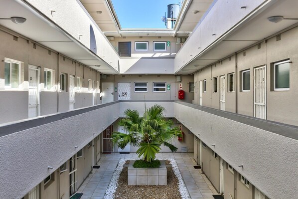 A hotel corridor with a central planter, multiple doors, and a clear sky view. - Sea Views by the Promenade at Oceanmist Studio (Cape Town)