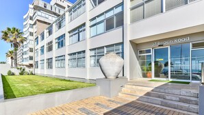 Un edificio moderno con un letrero que dice "37 Beach Road", con una amplia entrada de vidrio, un área pavimentada con escalones y un césped bien cuidado.