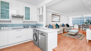 Una cocina moderna con armarios blancos, lavadora integrada y zona de comedor con sofá y mesa de centro.