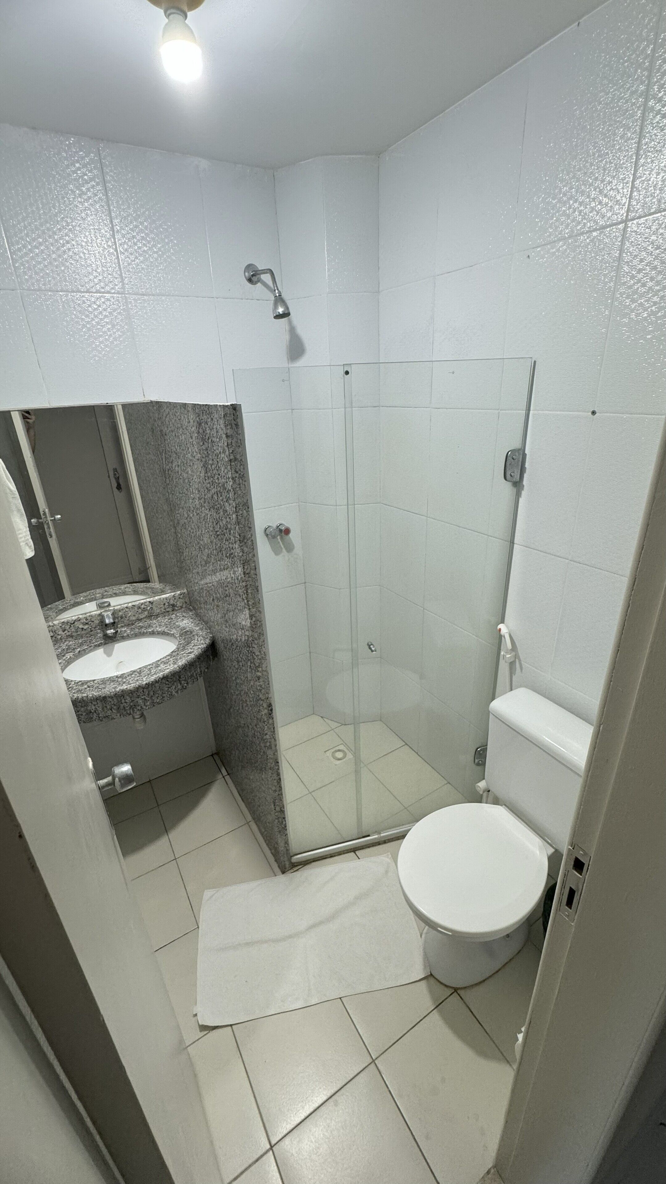 Un baño pequeño con lavamanos de granito, cabina de ducha de cristal y un inodoro blanco.