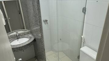 Un baño pequeño con lavamanos de granito, cabina de ducha de cristal y un inodoro blanco.