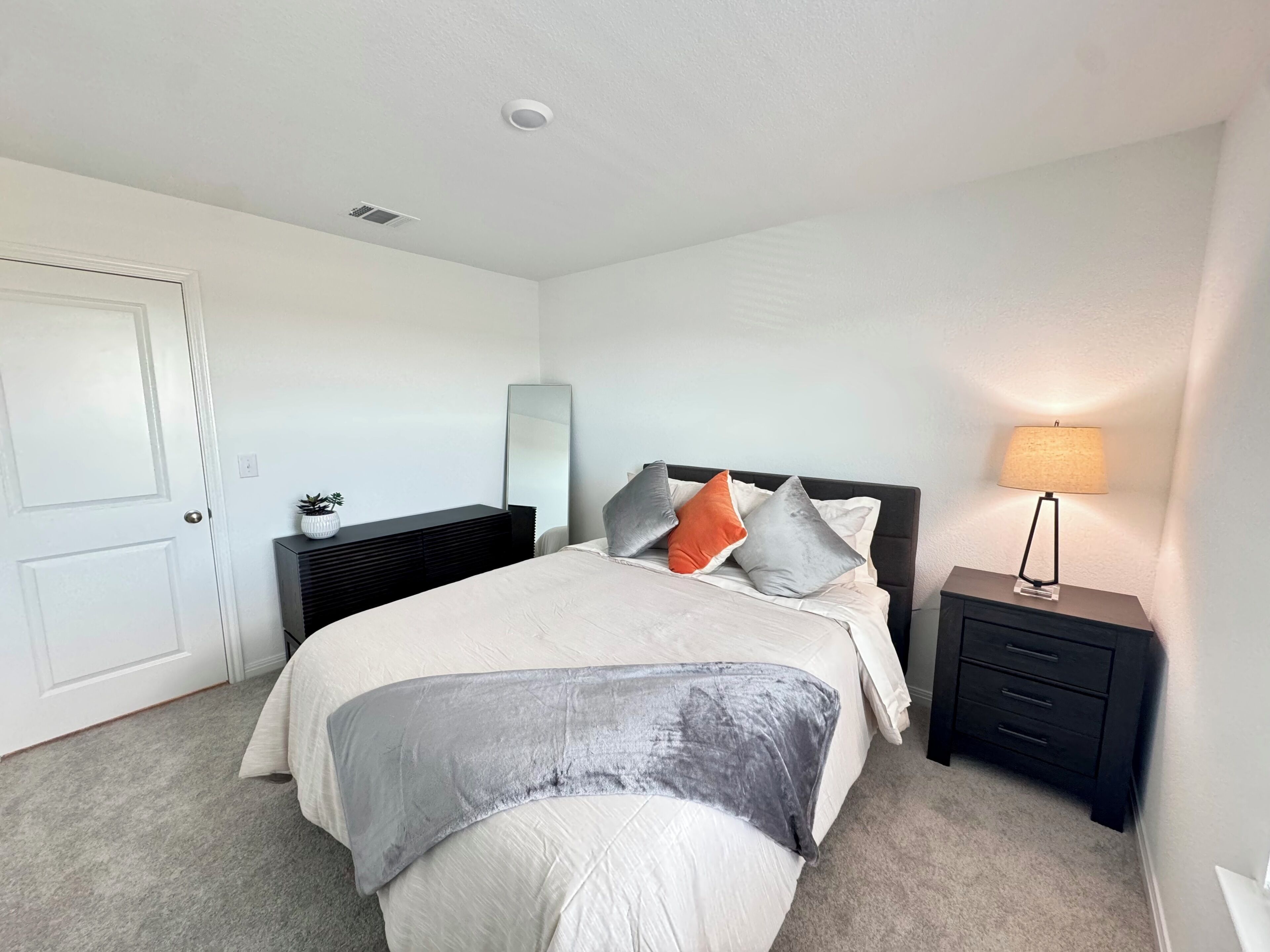 Une chambre à coucher avec un lit, des tables de chevet, une lampe, une commode et une porte.