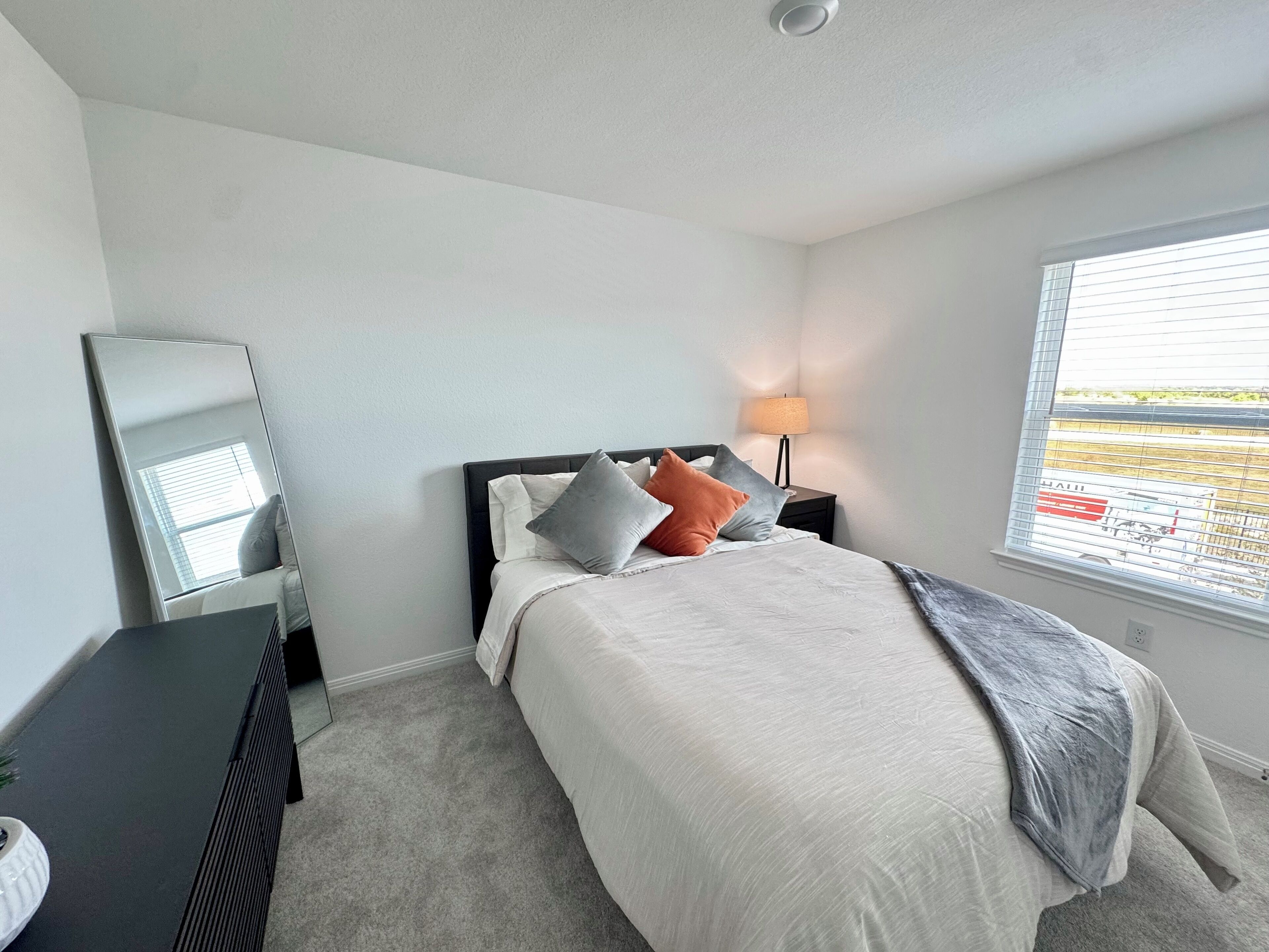 A neatly arranged bedroom with a bed, a bedside table, a lamp, and a window with blinds.
