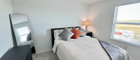 A neatly arranged bedroom with a bed, a bedside table, a lamp, and a window with blinds.