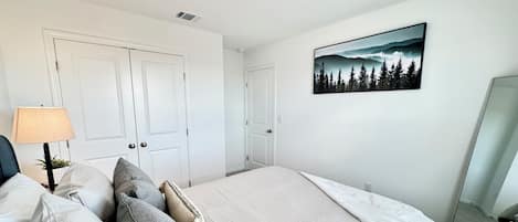 A bedroom with a bed, pillows, a lamp, a painting, and a mirror.