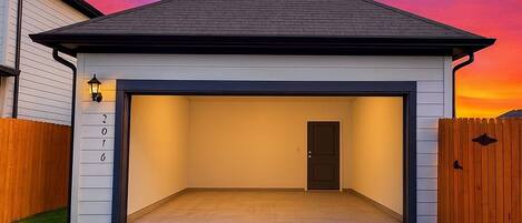 Una casa de un piso con garaje, techo oscuro y fachada de color claro.