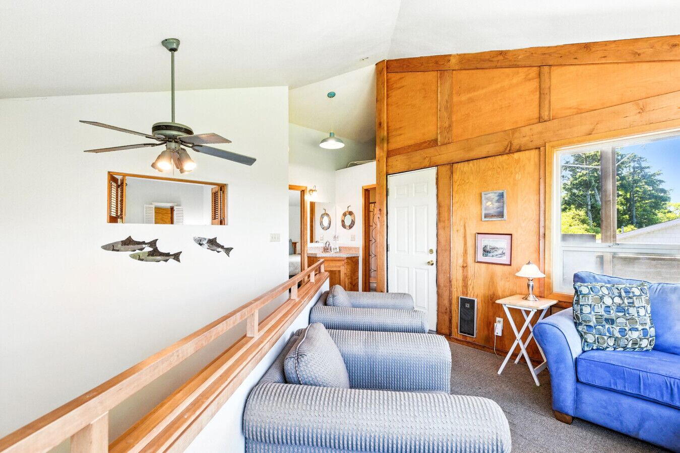 A cozy living room with a wooden ceiling, a blue sofa, and a staircase leading to another room.