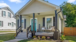 A single-story house with a front porch, a green door, and a welcome sign.
