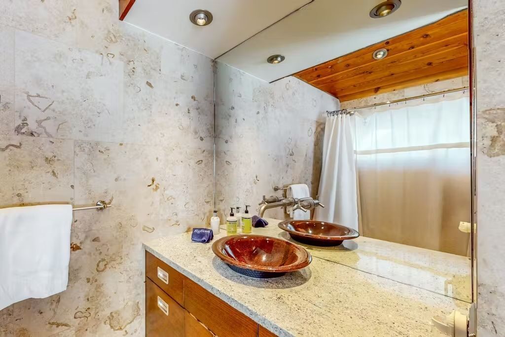 A bathroom with a marble wall, wooden ceiling, two sinks, and a large mirror.