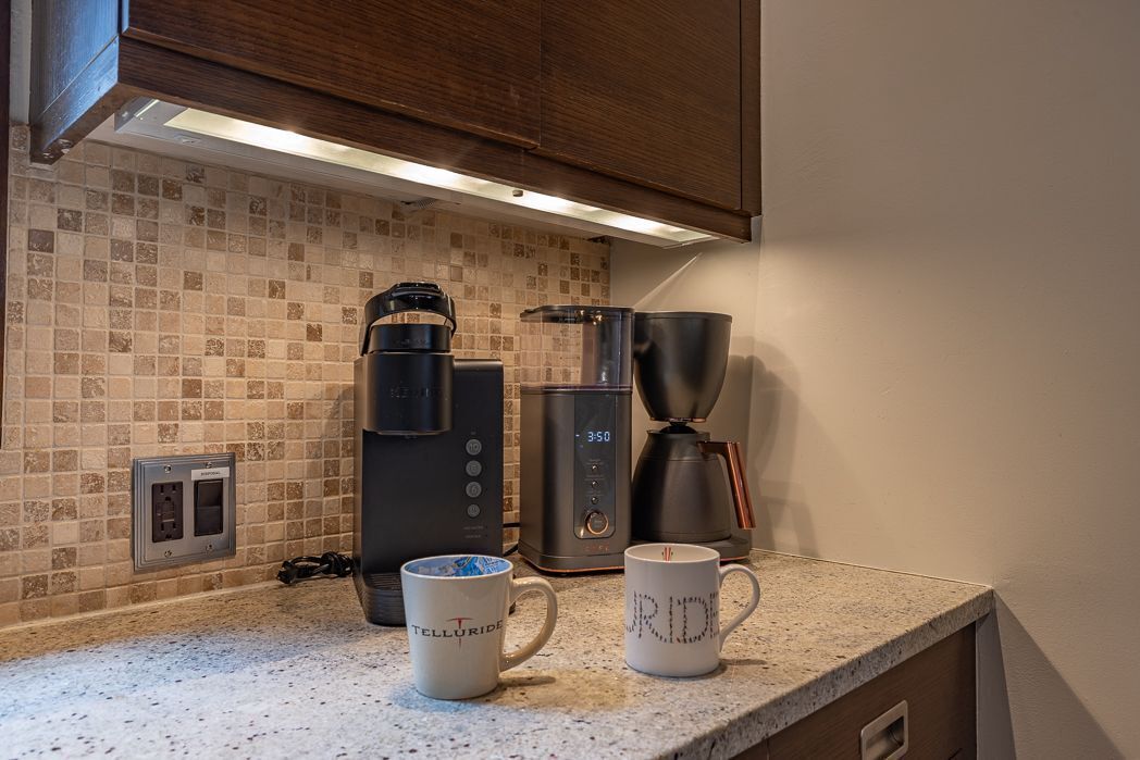 A kitchen with a coffee maker, a kettle, and two mugs on the counter.