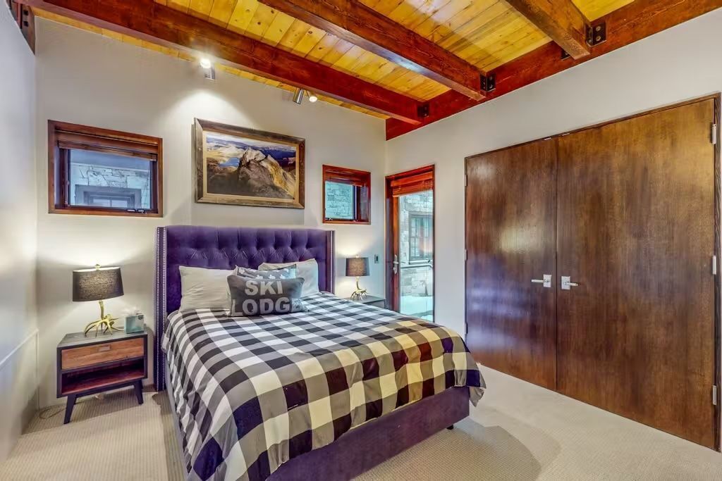 A bedroom with a checkered bedspread, a large wooden wardrobe, and a painting on the wall.