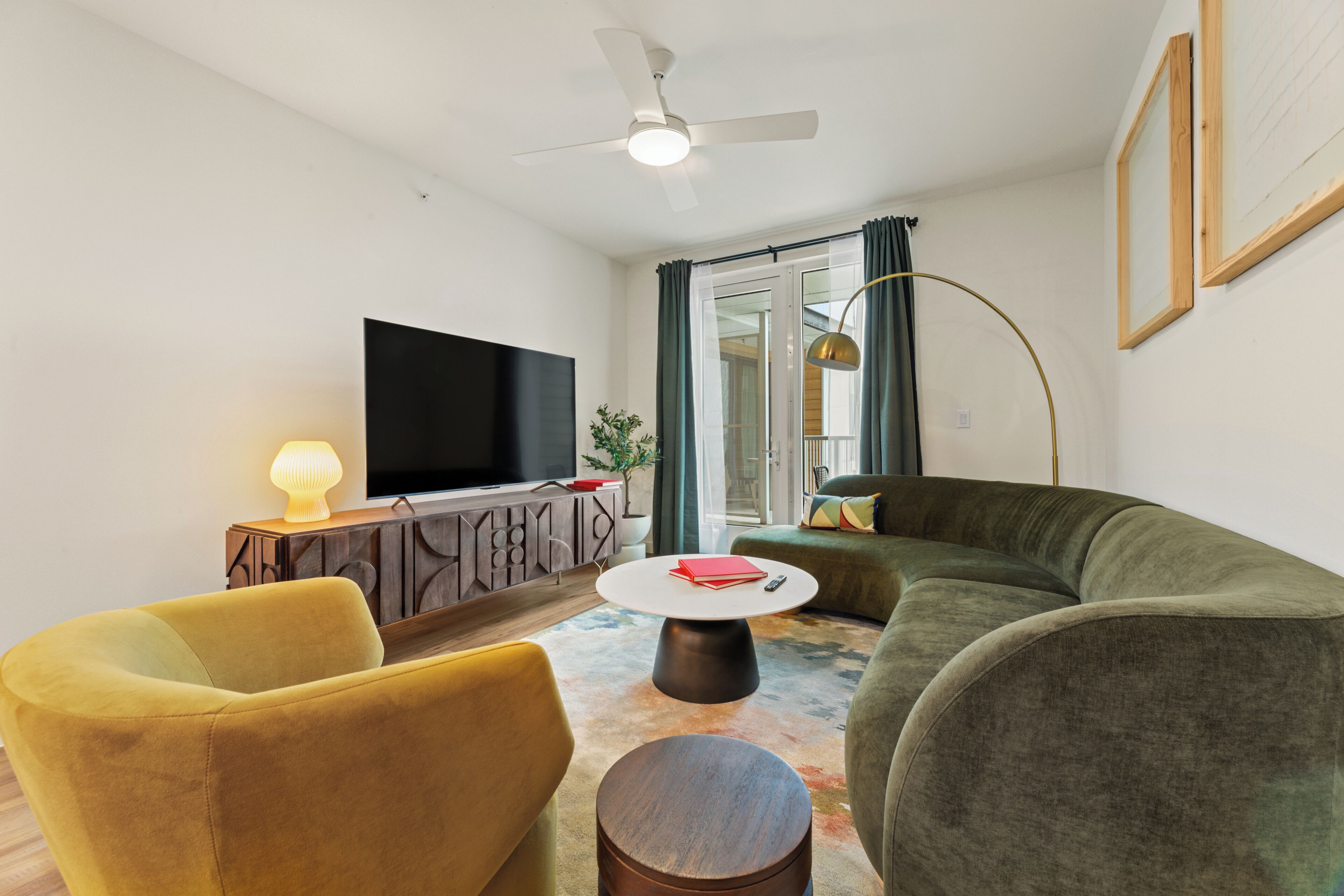 Ein Wohnzimmer mit Flachbildfernseher, einer Couch, einem gelben Sessel, einem Couchtisch und einem Deckenventilator.