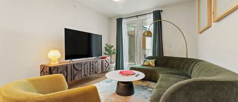 Ein Wohnzimmer mit Flachbildfernseher, einer Couch, einem gelben Sessel, einem Couchtisch und einem Deckenventilator.