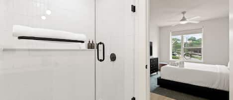 Un bagno moderno con cabina doccia in vetro, un porta asciugamani bianco e una finestra visibile nella stanza adiacente.
