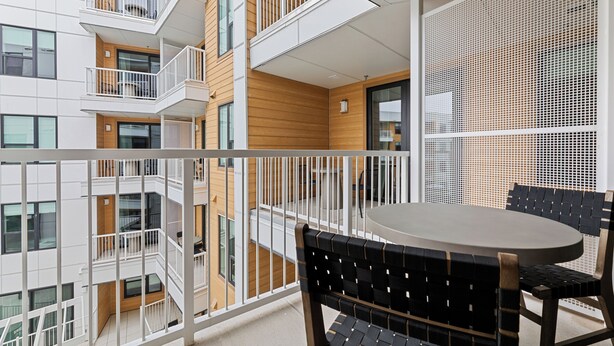 A balcony with a table and chairs, a white railing, and a view of adjacent buildings.