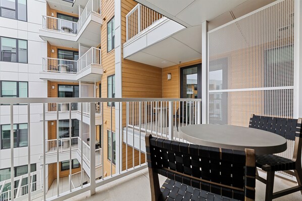 A balcony with a table and chairs, a white railing, and a view of adjacent buildings.