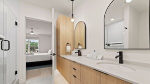 A modern bathroom with a large mirror, two sinks, wooden cabinets, and a shower area.