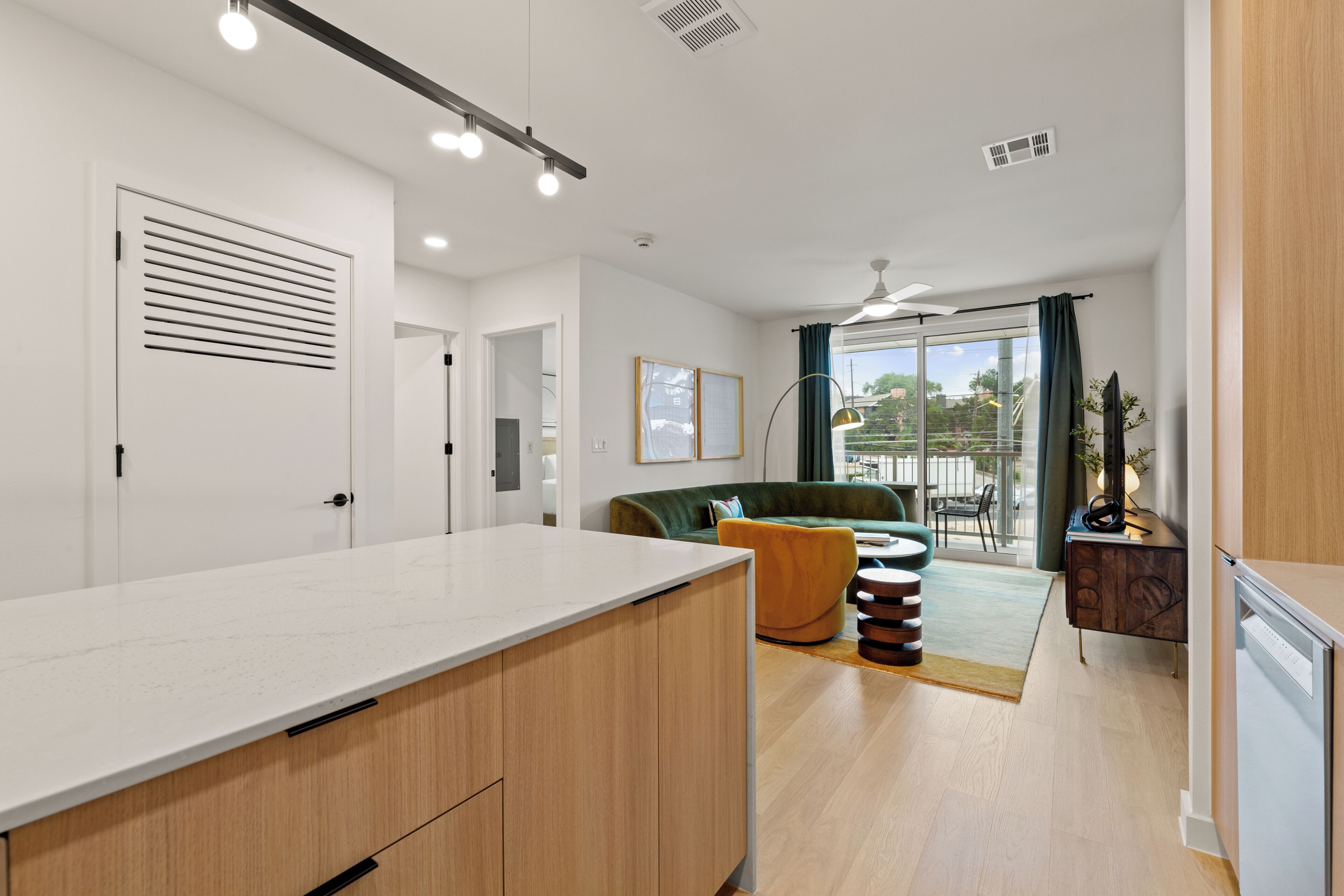 A modern kitchen with a white countertop and wooden cabinets, a green sofa, and a dining area with a table and chairs.