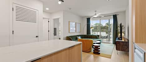 A modern kitchen with a white countertop and wooden cabinets, a green sofa, and a dining area with a table and chairs.