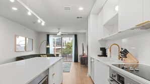 Une cuisine moderne avec des meubles blancs, un îlot central, un four encastré et un coin repas offrant une vue agréable.