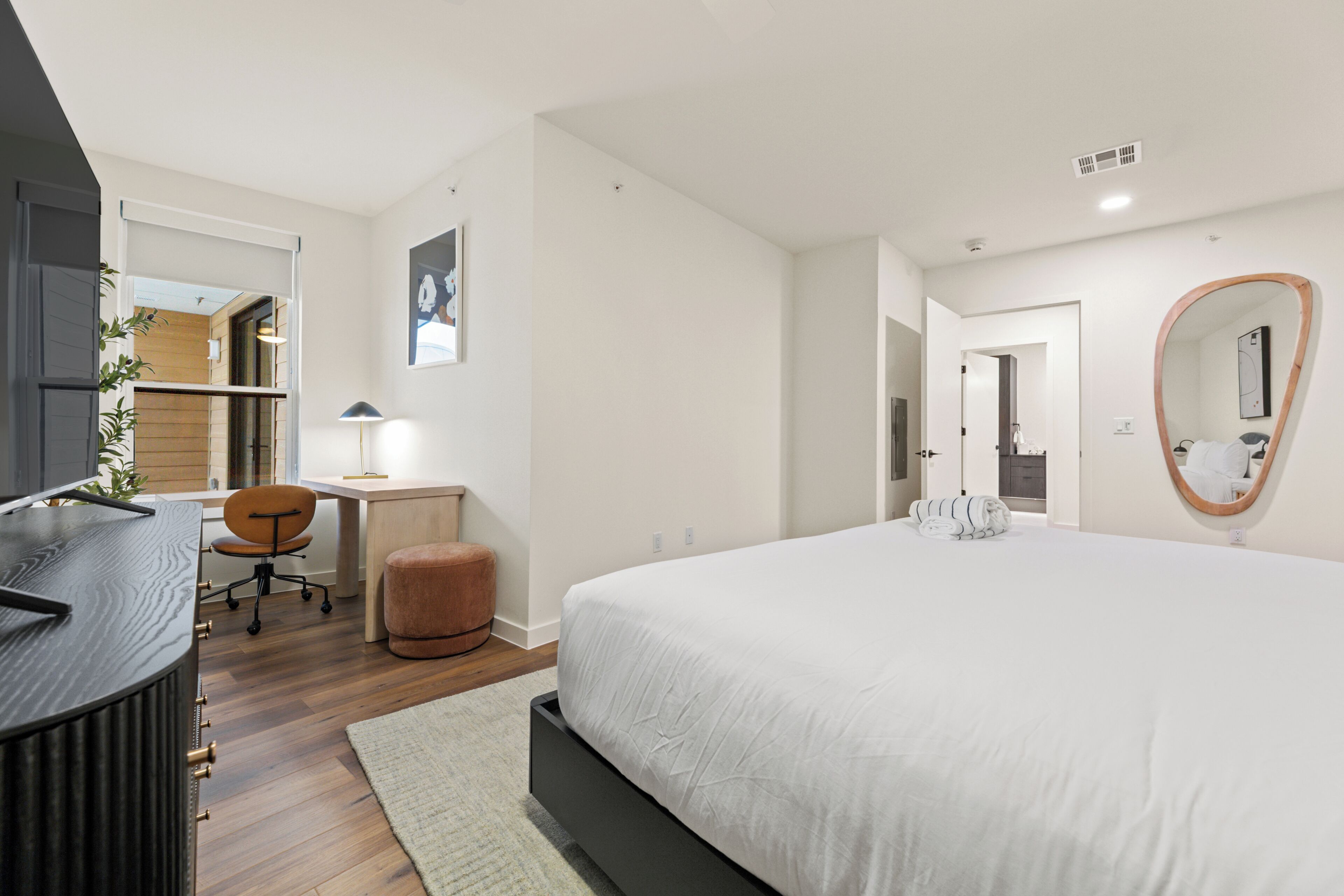A modern bedroom with a large bed, a desk, a chair, and a mirror.