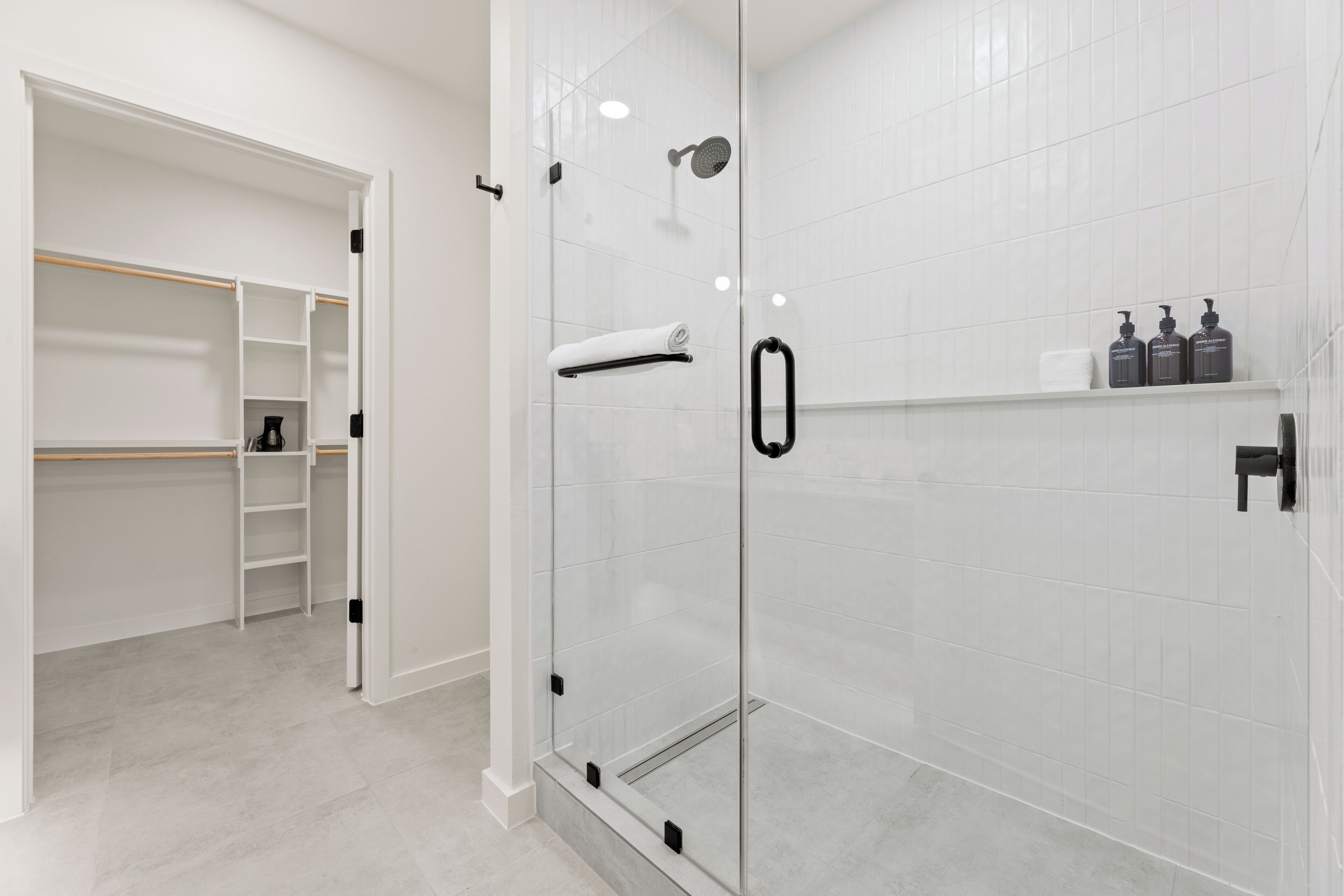 A modern bathroom with a glass shower enclosure, a white tiled wall, and a built-in shelf with toiletries.
