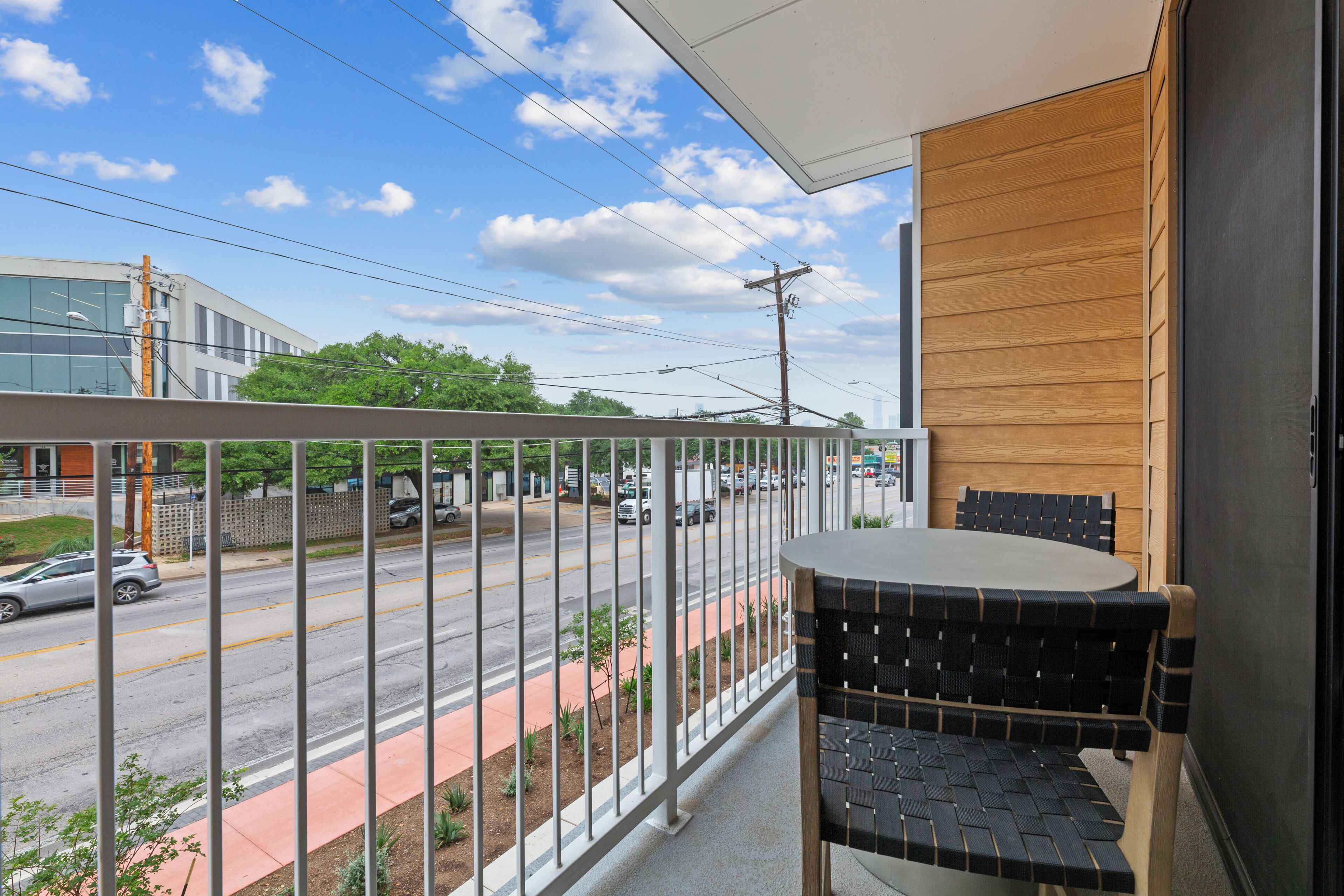 A balcony with a table and chairs, overlooking a street with cars and buildings.