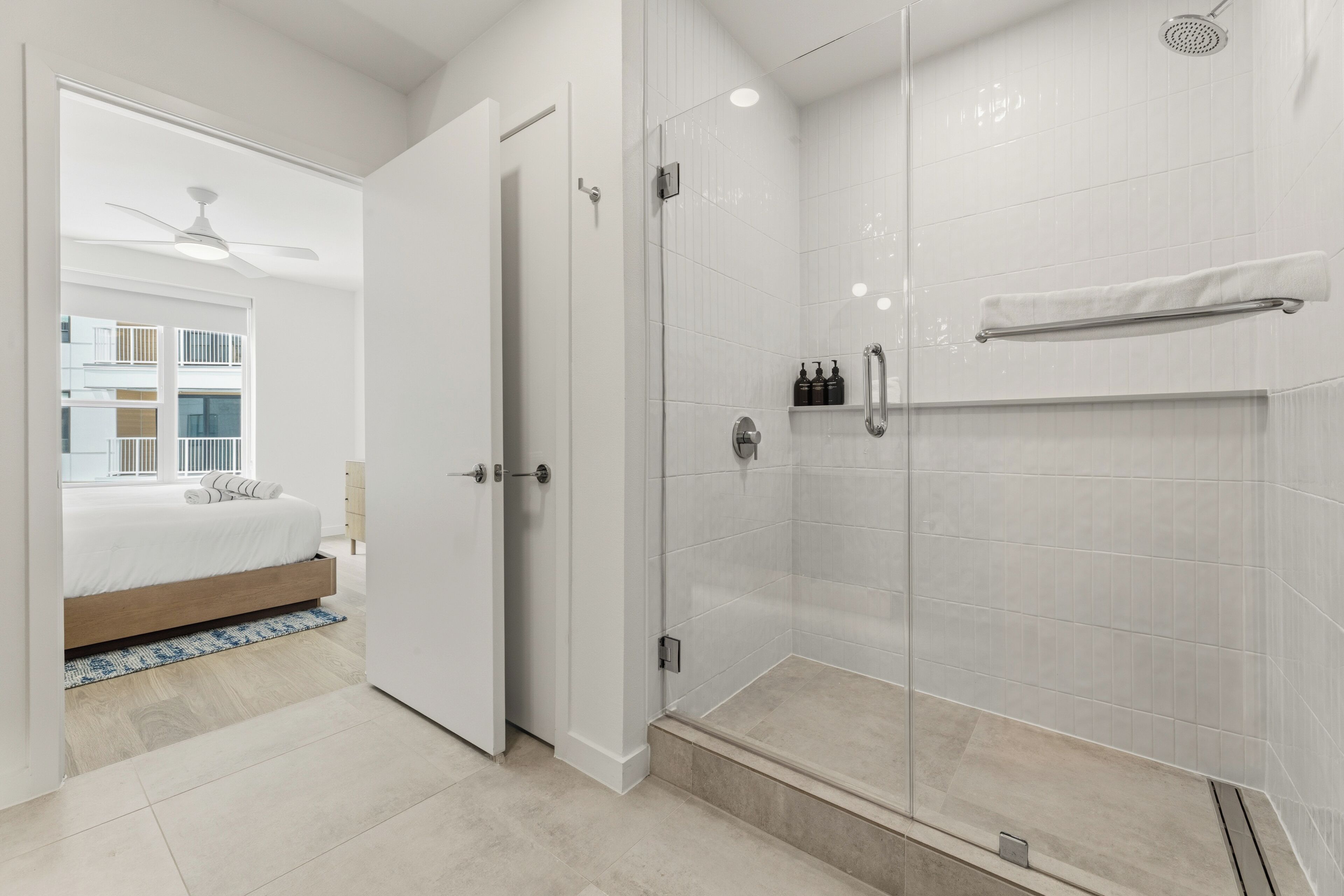 A modern bathroom with a glass shower enclosure, a white towel rack, and a visible bottle of shampoo.
