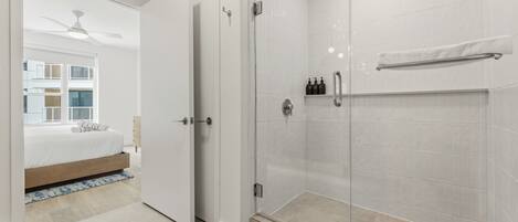 A modern bathroom with a glass shower enclosure, a white towel rack, and a visible bottle of shampoo.