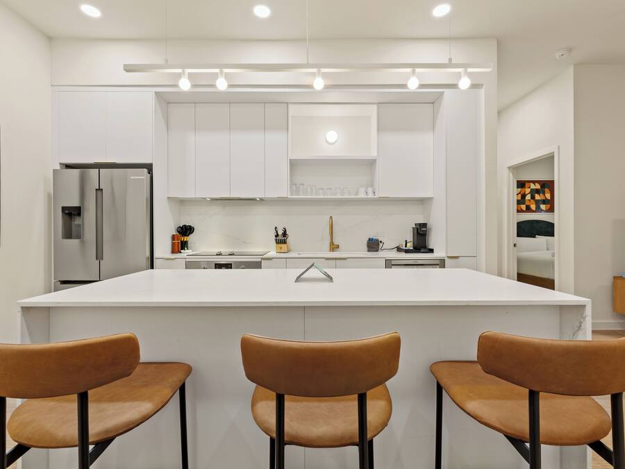 A modern kitchen with white cabinetry, a central island with bar stools, and a stainless steel refrigerator.