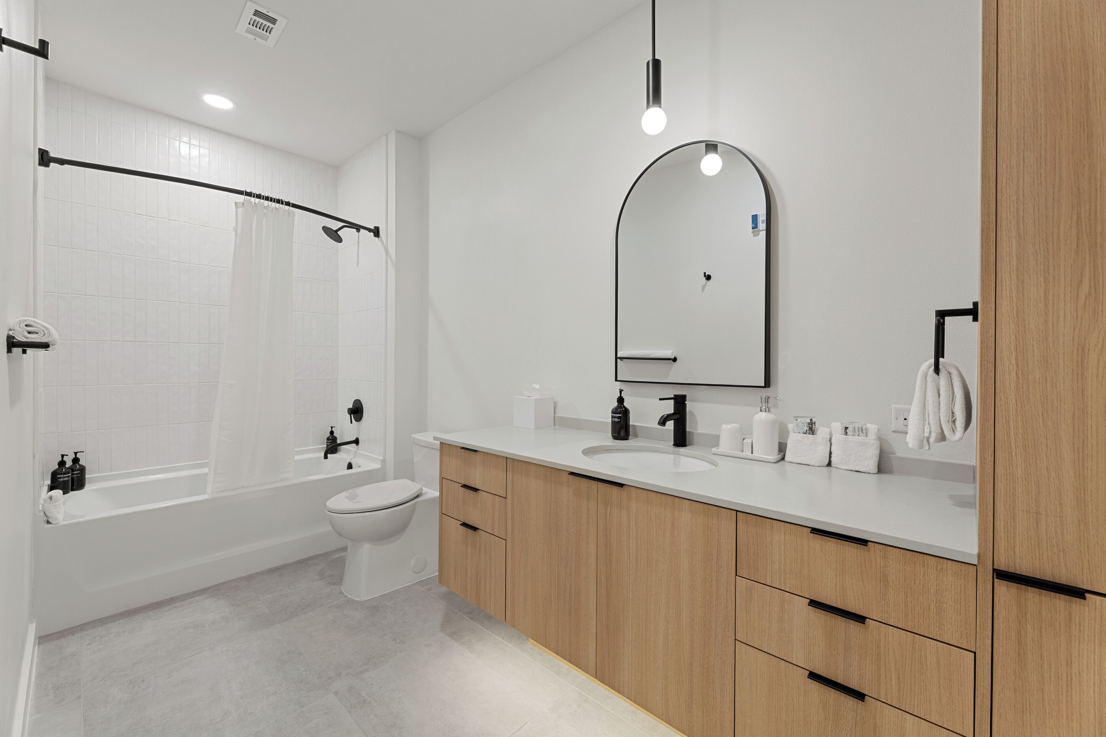 Un baño moderno con bañera, inodoro, tocador y un espejo grande.