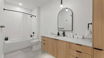 Un baño moderno con bañera, inodoro, tocador y un espejo grande.