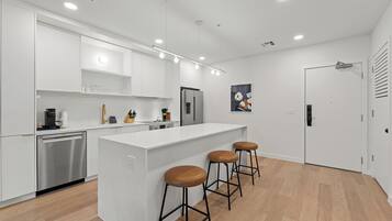 Una cocina moderna con armarios blancos, lavavajillas de acero inoxidable, refrigerador y una isla central con taburetes.