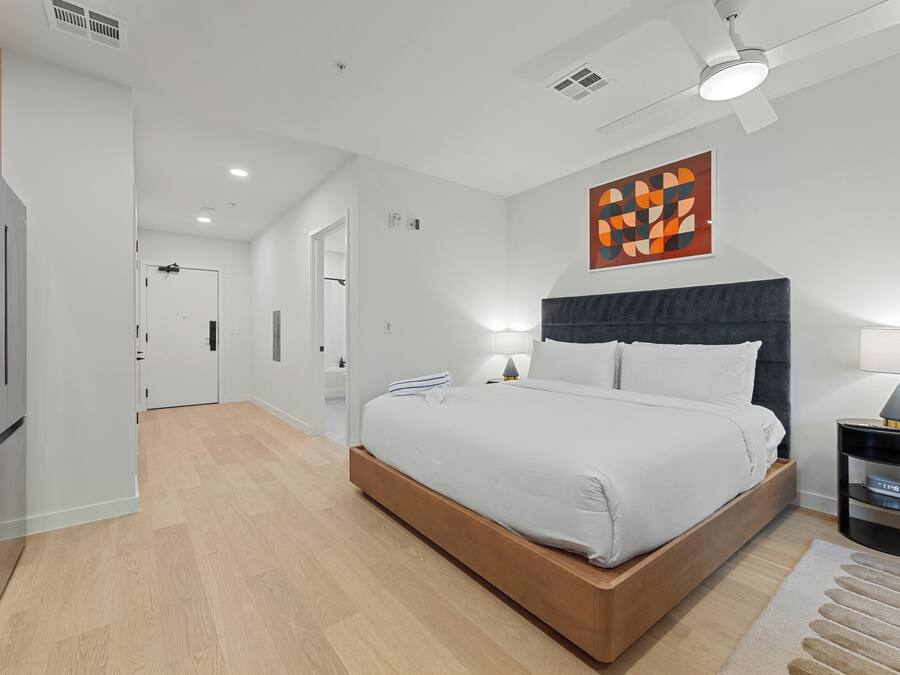 Un dormitorio moderno con cama, lámparas de noche, ventilador de techo y una obra de arte en la pared.