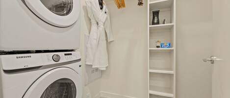 A laundry area with a Samsung washing machine, a drying rack, and a white robe hanging.
