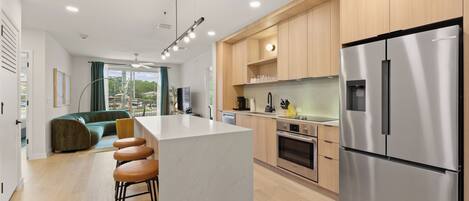 A modern kitchen with a central island, stainless steel appliances, wooden cabinets, and a seating area with a sofa and bar stools.