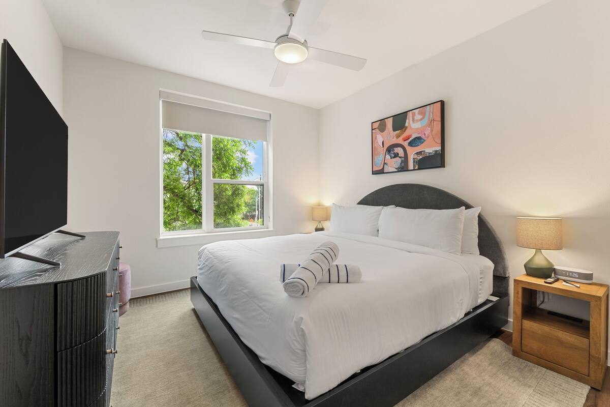 Un dormitorio moderno con cama, mesita de noche, ventana y ventilador de techo.