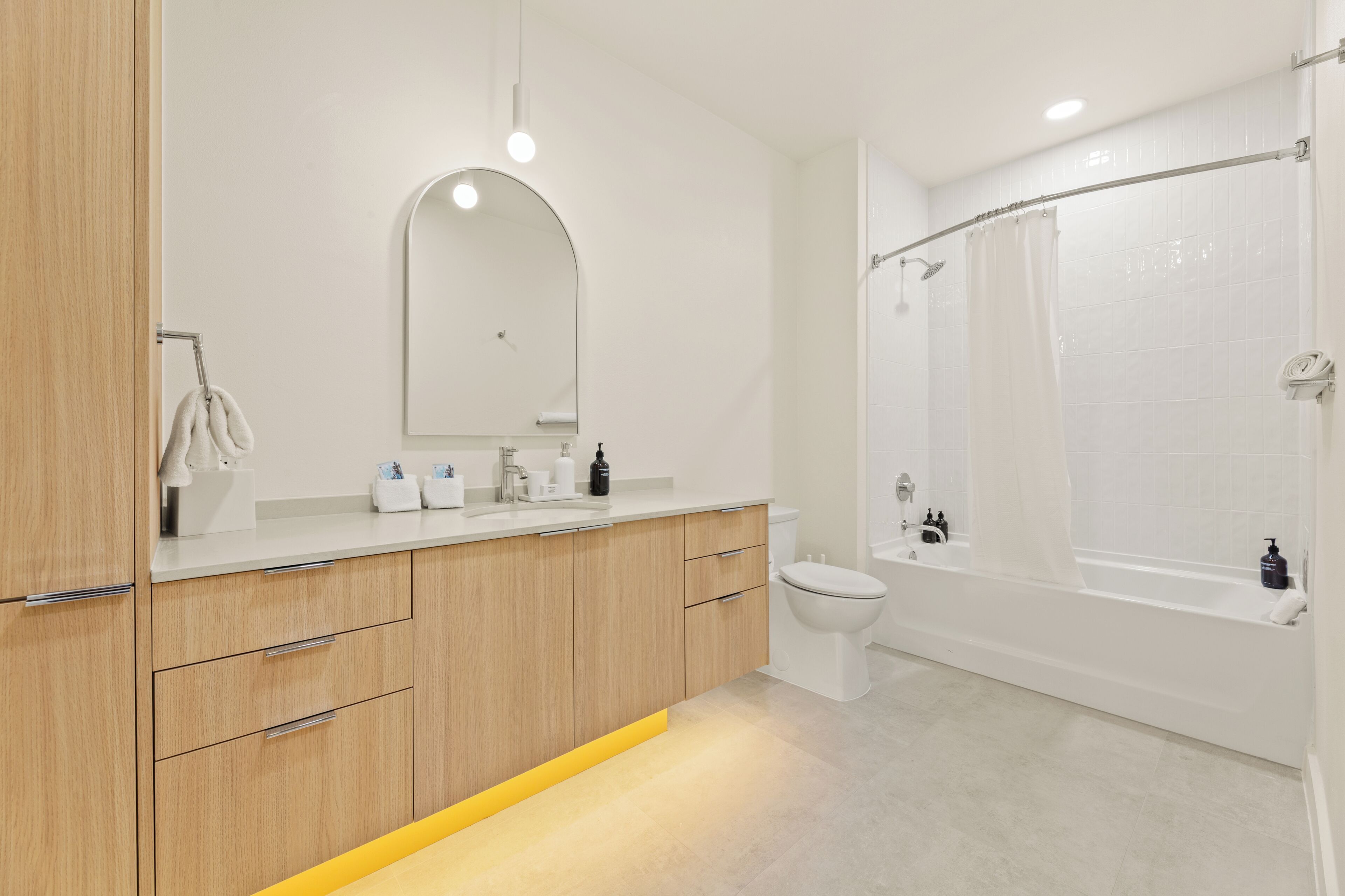 A modern bathroom with a wooden vanity, a large mirror, a toilet, and a bathtub.