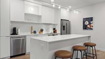 A modern kitchen with white cabinetry, a stainless steel dishwasher, a refrigerator, and a central island with stools.